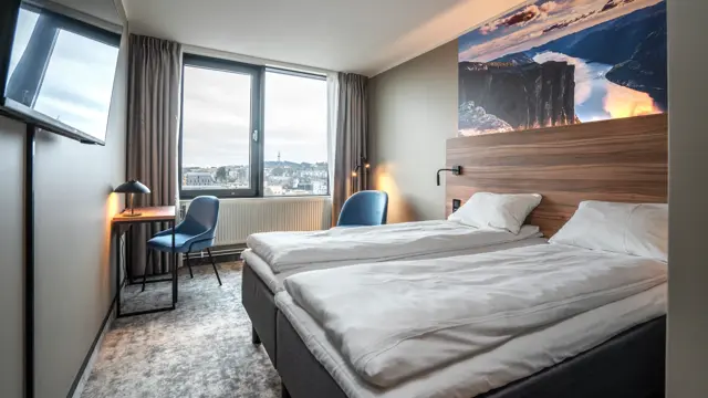 Twinrom med to enkeltsenger, hvilestoler, skrivebord med lampe, TV, vinduer, teppebelagt gulv, sengegavl i tre og panoramabilde av Lysefjorden.