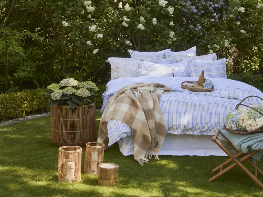 Lexington oppredd seng ute på gress, hortensia i kurv på siden, lyslykter og krakk med blomsterkurv 