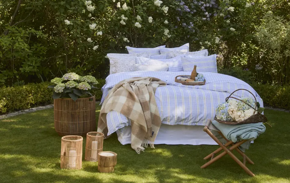 Lexington oppredd seng ute på gress, hortensia i kurv på siden, lyslykter og krakk med blomsterkurv 