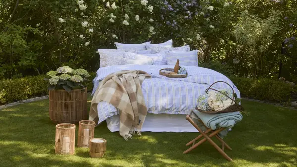 Lexington oppredd seng ute på gress, hortensia i kurv på siden, lyslykter og krakk med blomsterkurv 