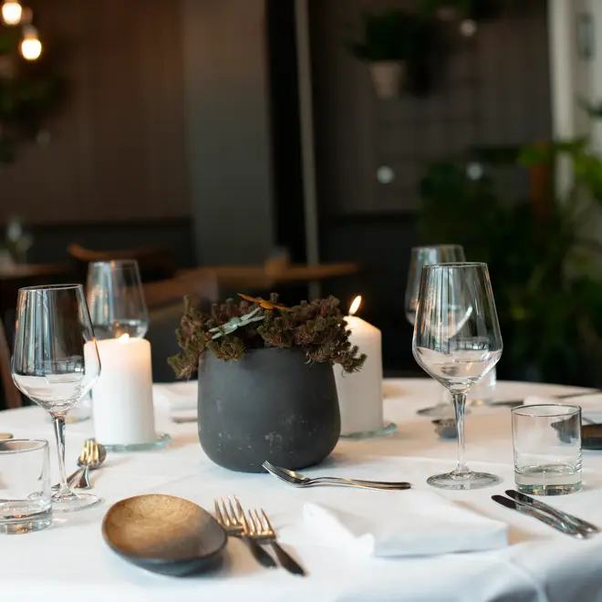 Bord dekket med hvit duk og servise. Svart blomsterpotte stående på midten av bordet. 