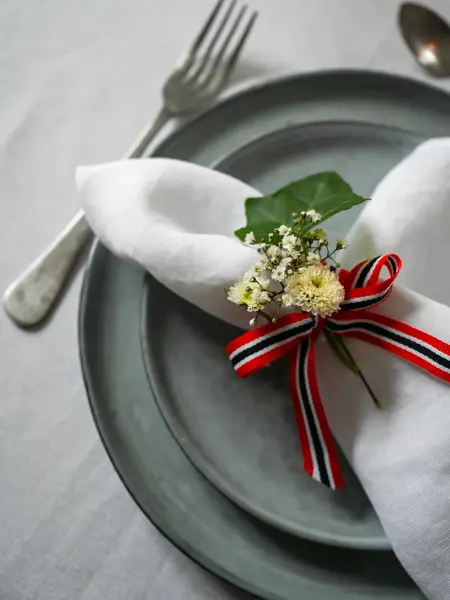 Nærbilde av kurvert med grått service, linserviett med 17. mai-bånd og blomster.