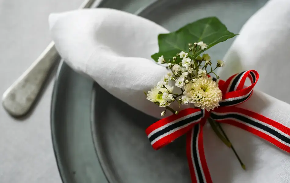 Nærbilde av kurvert med grått service, linserviett med 17. mai-bånd og blomster.