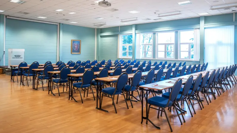 Klasseromoppsett, vindu, projektor, turkise vegger, parkettgulv, blå stoler. 