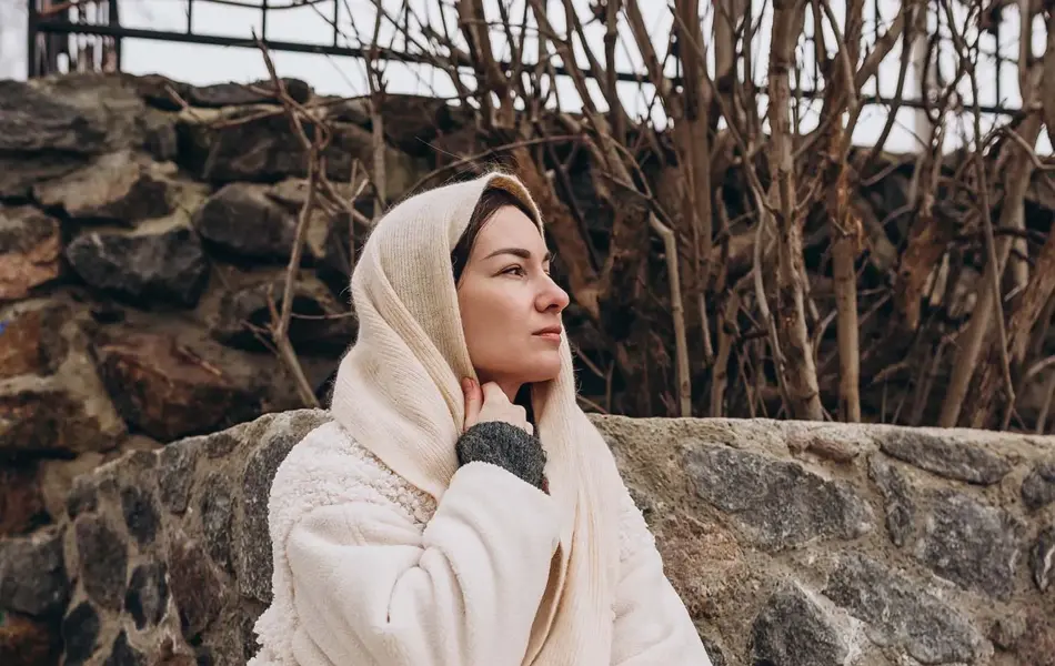 En dame med hvit fluffy jakke og brune boots sitter i en park