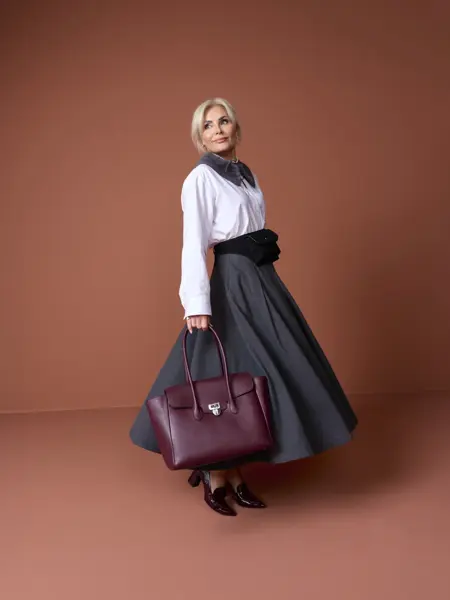 Marianne i hvit skjorte, skjerf, grått skjørt, veske og pumps.