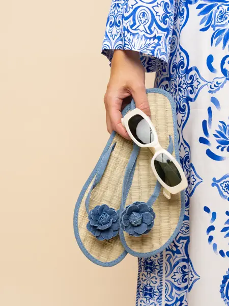 Hånd holder blå flip flops og hvite solbriller