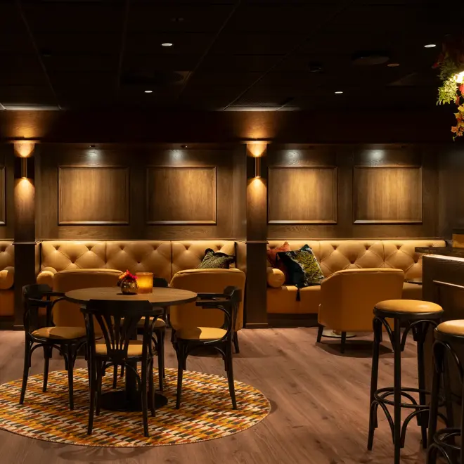 Dempet belysning i lobbyområdet med sofa langs veggen og runge bord med stoler rundt