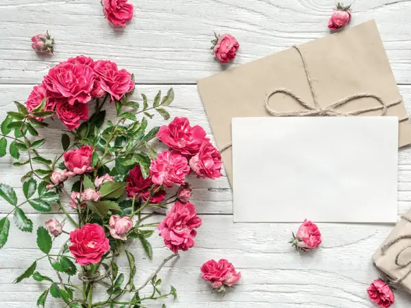 blank white greeting card and gift box with pink rose flowers bouquet on white wooden table. mock up. top view. valentines day background. vintage toning