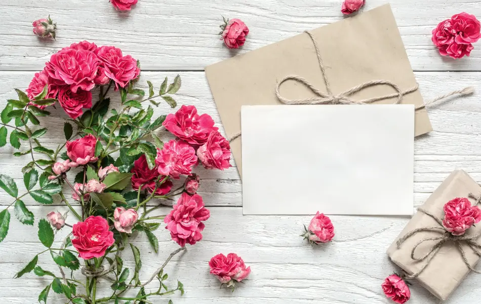 blank white greeting card and gift box with pink rose flowers bouquet on white wooden table. mock up. top view. valentines day background. vintage toning
