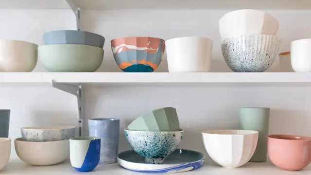 To hvite hyller med kopper, kar og fat i fargerik keramikk