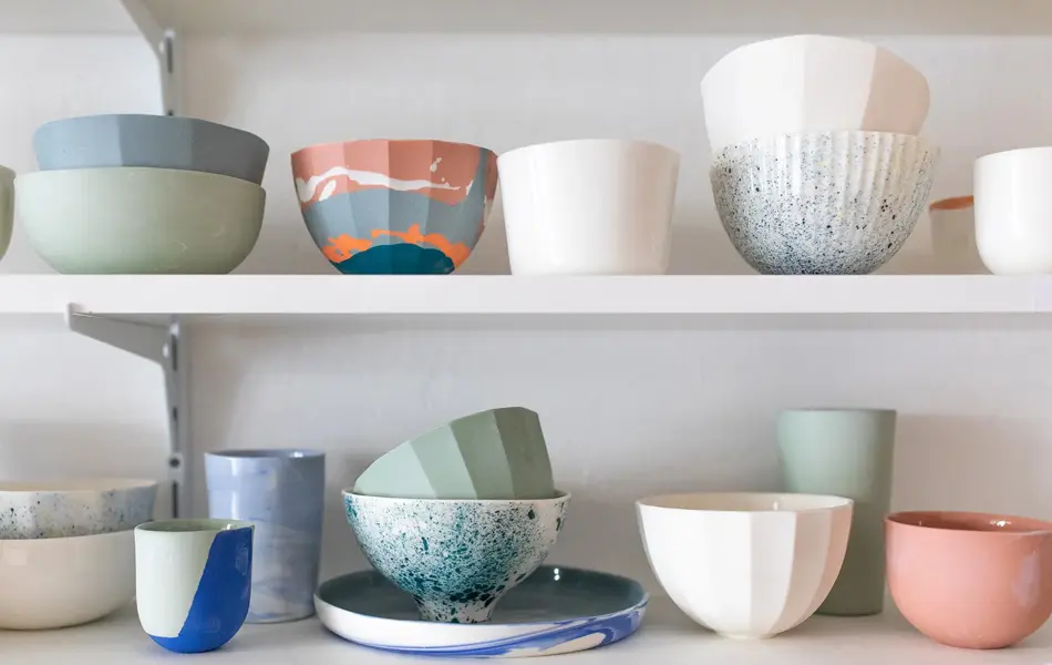 To hvite hyller med kopper, kar og fat i fargerik keramikk