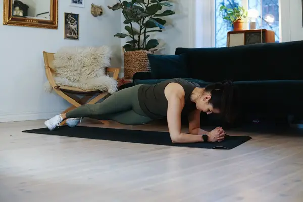 treningsekspert Anna Johansen trener på matte på gulvet, mørkegrønn sofa i bakgrunnen, lys stol med pels oppi, str grønn plante, bilder på veggen