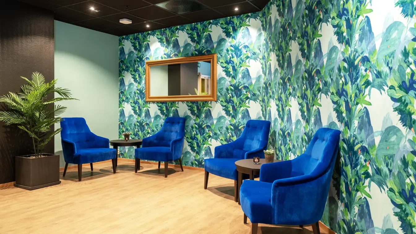 Fargerik tapetvegg, fire mørkeblå lenestoler, salongbord, parkettgulv, plante