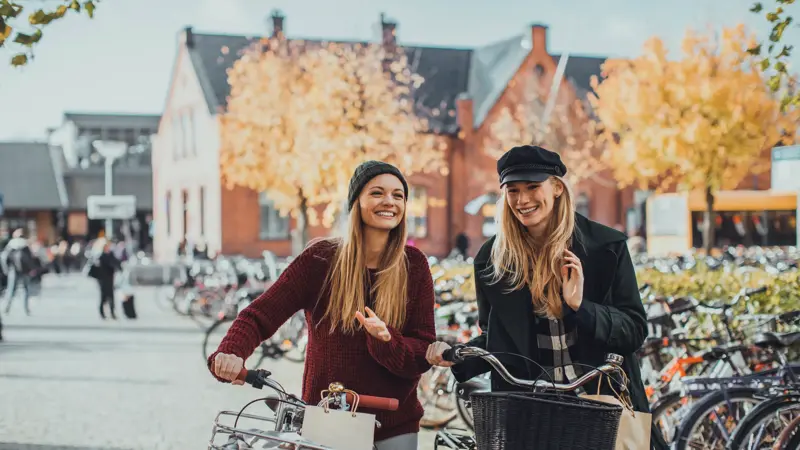Photo of a young women leading their bikes through city