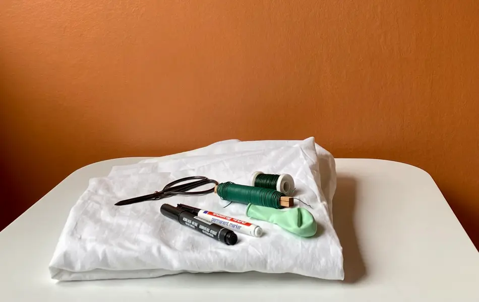 Hvit laken, tusj, tråd, balong og saks som ligger på et bord med oransje bakgrunn