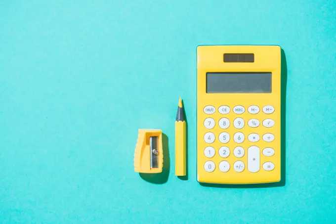 top view of arrangement of calculator, pencil and pencil sharpener on blue backdrop