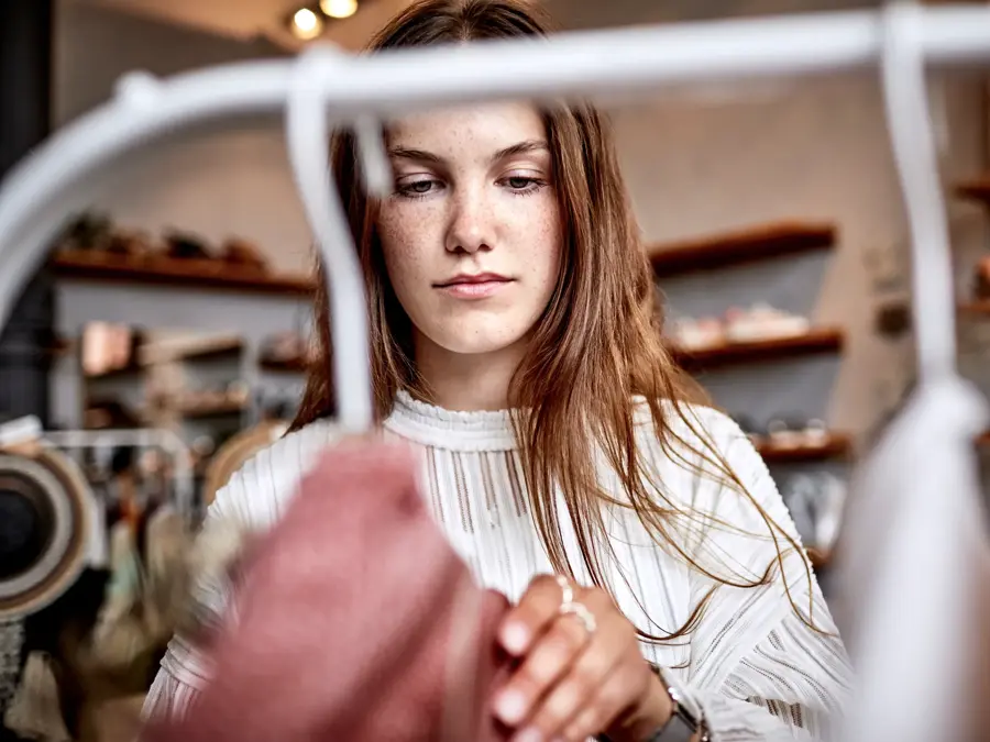 brunette kikker på klesstativ i butikk