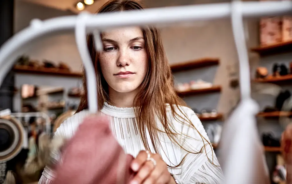 brunette kikker på klesstativ i butikk