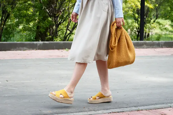 Summer fashion outfit. Girl in dress, yellow shoes and trendy knitted bag, a side view
