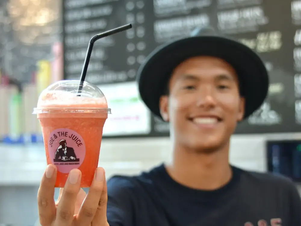 Smilende mann med sort hatt som holder en oransje juice med sugerør