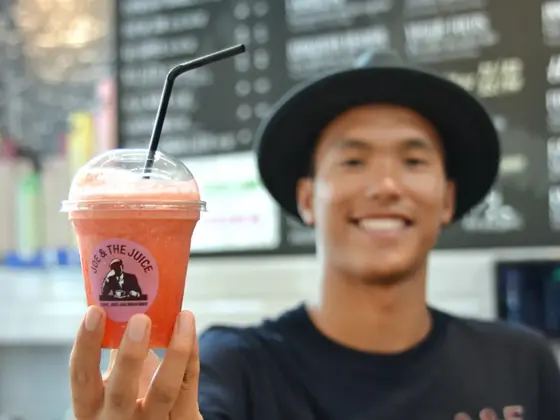 Smilende mann med sort hatt som holder en oransje juice med sugerør