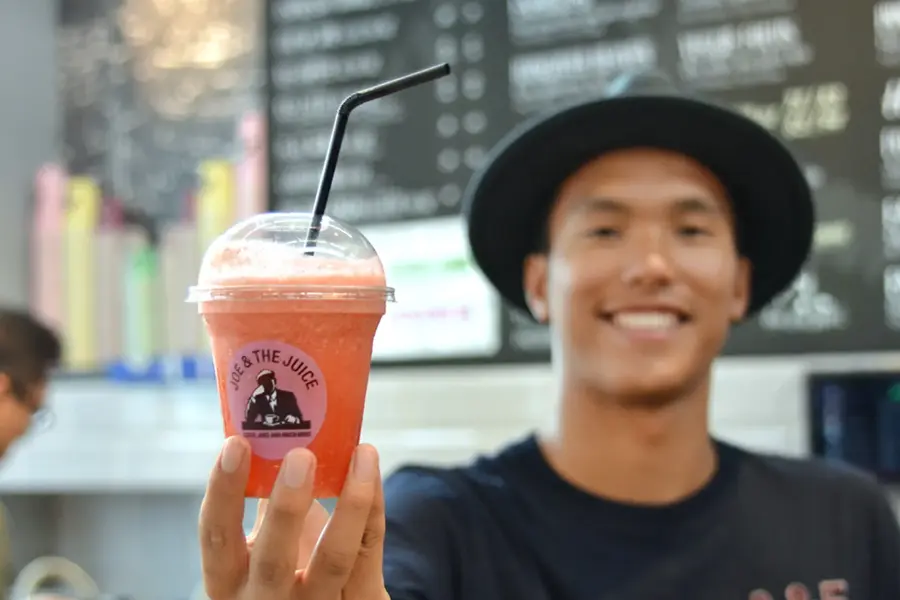 Smilende mann med sort hatt som holder en oransje juice med sugerør