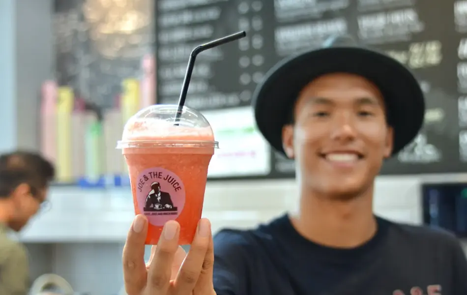 Smilende mann med sort hatt som holder en oransje juice med sugerør