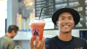 Smilende mann med sort hatt som holder en oransje juice med sugerør
