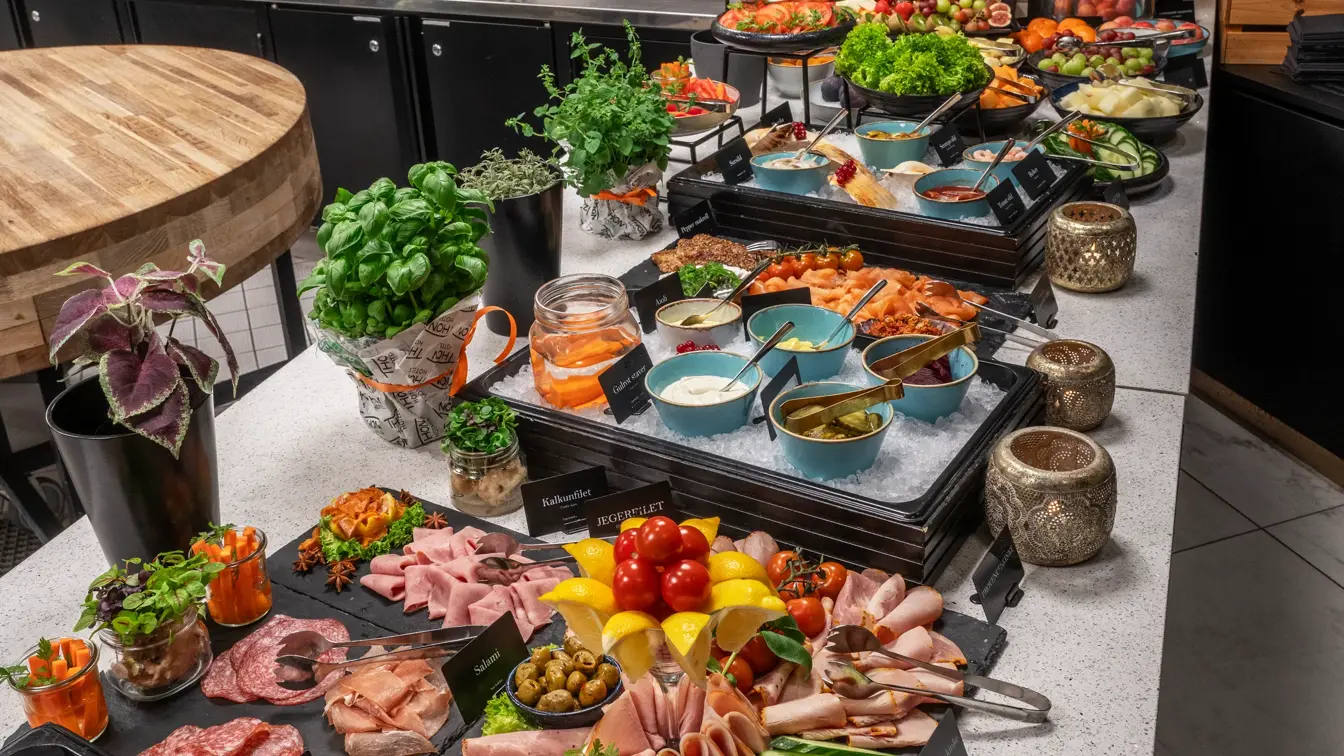 Frokostbuffet med fargerikt utvalg av pålegg, oppkuttede grønnsaker, urteplanter og frukt