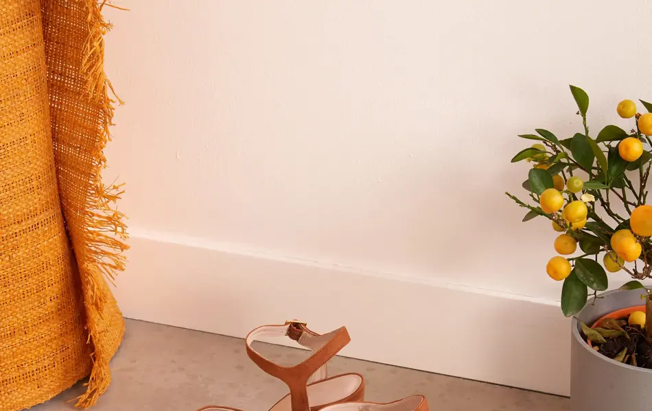 Brune semsket sandaler med hæl og åpen tå, med appelsinplante og oransje teppe i bakgrunnen.