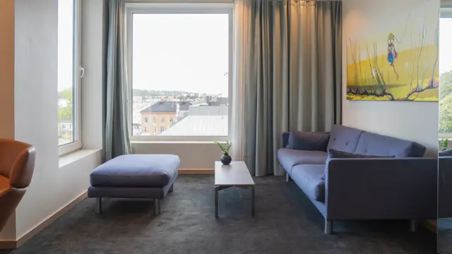 Sittegruppe i junior suite med sofa, sofabord, puff, store vinduer med gardiner.