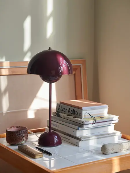 Burgunder flowerpot bordlampe står på en lite bord.