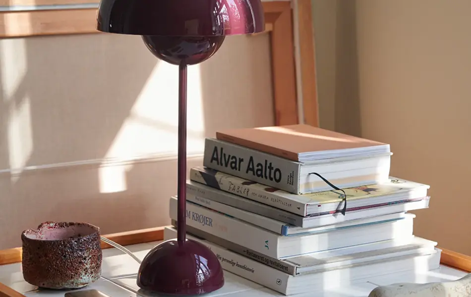 Burgunder flowerpot bordlampe står på en lite bord.