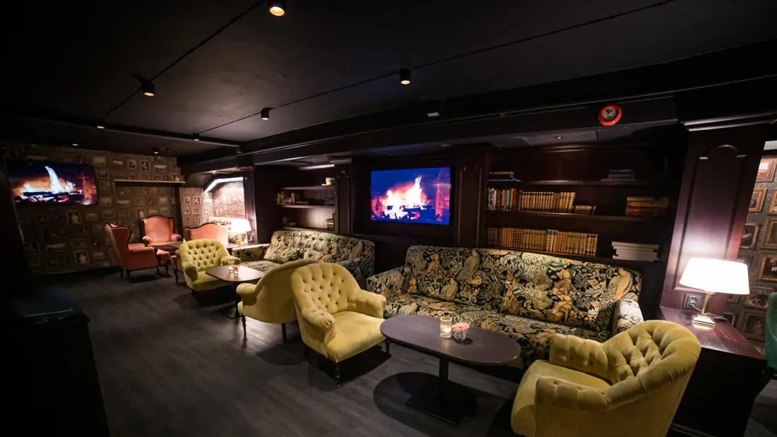 Parkettgulv, grønn loungegruppe, bokhulle og tv med peis