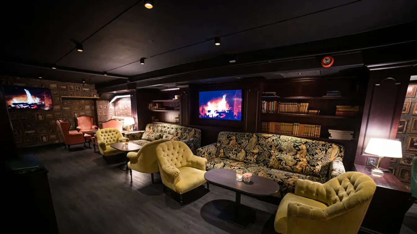 Parkettgulv, grønn loungegruppe, bokhulle og tv med peis