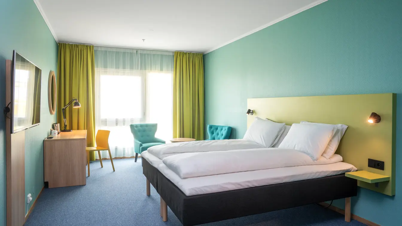 Turkise vegger, vindu, skrivebord, gul stol, turkis stol, salongbord, dobbeltseng.