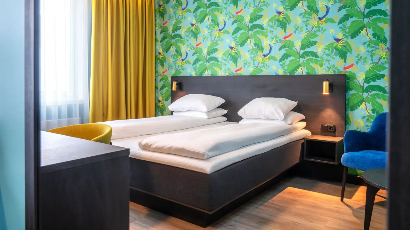 Grønn tapetvegg med mønster, gule gardiner, dobbeltseng, parkettgulv, blå stol, skrivebord, vindu