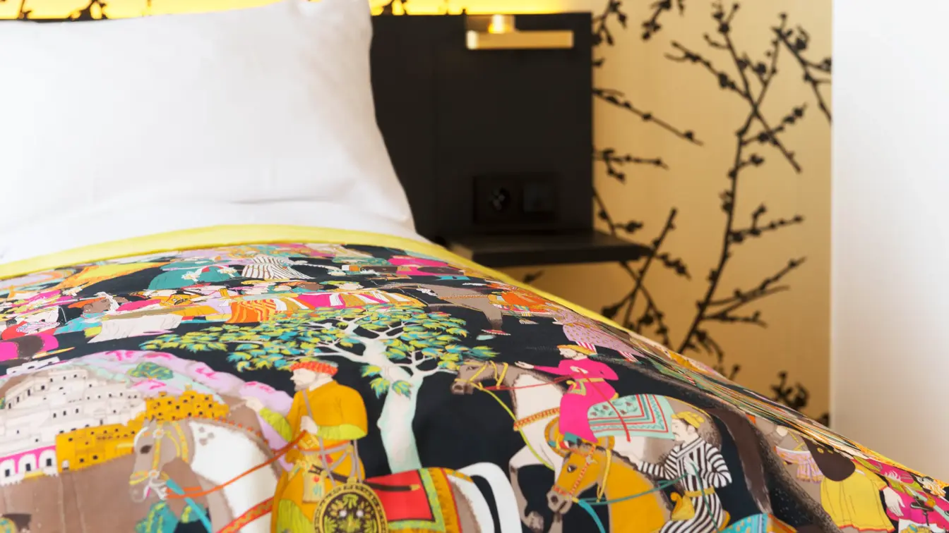 Dobbeltseng detaljbilde med mønstret gulltapet og fargerikt sengeteppe i room på Thon Hotel Rosenkrantz Oslo, som ligger i Oslo sentrum