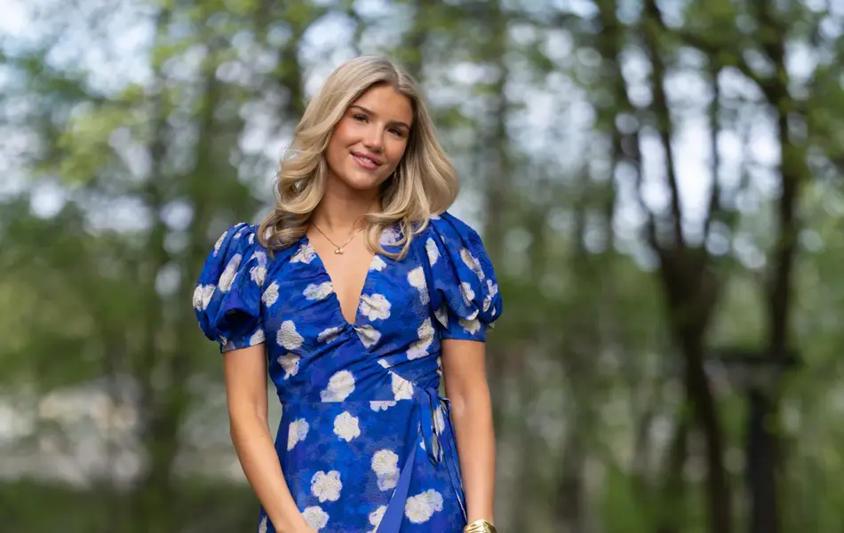 Ung jente i lang blå blomstrete kjole, sandaler og hvit håndveske