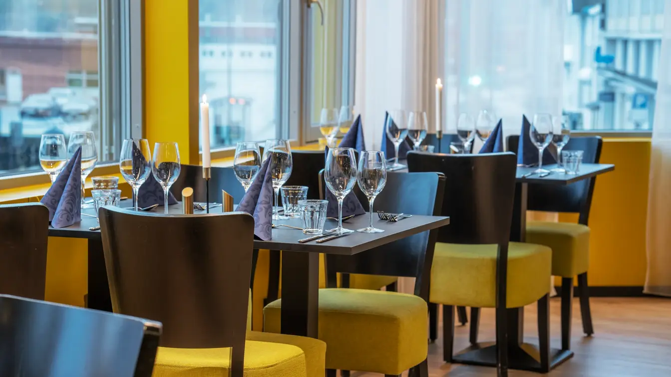 Svarte spisebord med svarte og gule stoler, og fire store vinduer.