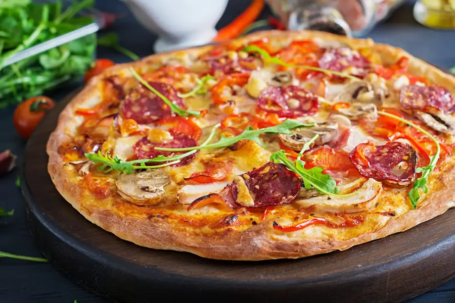 Fresh Italian pizza with chicken fillet, mushrooms, ham, salami, tomatoes, cheese on a black background. Italian food.