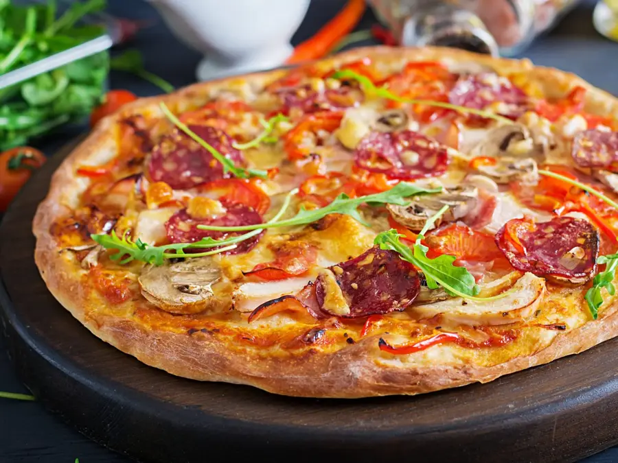 Fresh Italian pizza with chicken fillet, mushrooms, ham, salami, tomatoes, cheese on a black background. Italian food.
