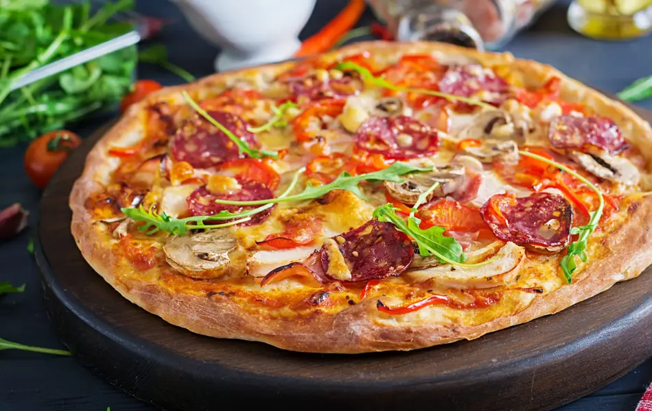 Fresh Italian pizza with chicken fillet, mushrooms, ham, salami, tomatoes, cheese on a black background. Italian food.