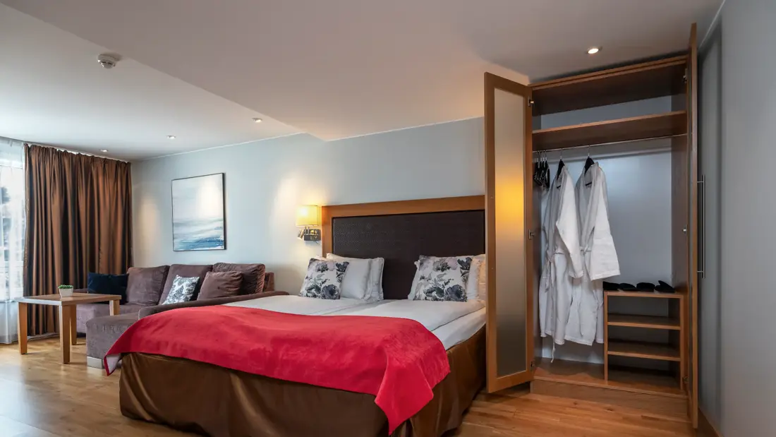 Superior rom med dobbeltseng, rødt sengeteppe, garderobeskap, sittegruppe ved vindu og parkettgulv.