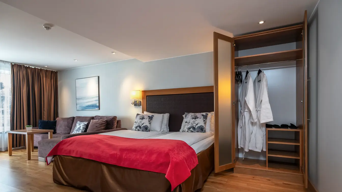 Superior rom med dobbeltseng, rødt sengeteppe, garderobeskap, sittegruppe ved vindu og parkettgulv.