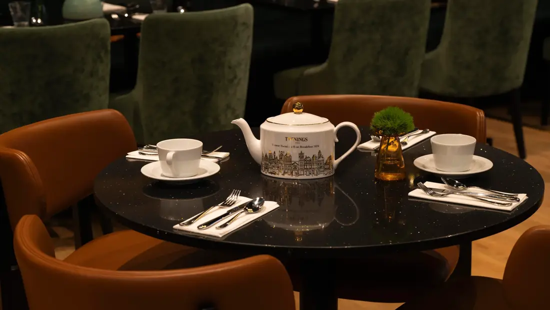 Twinings tekanne plassert på et rundt bord i en restaurant dekket med hvite kopper og bestikk.