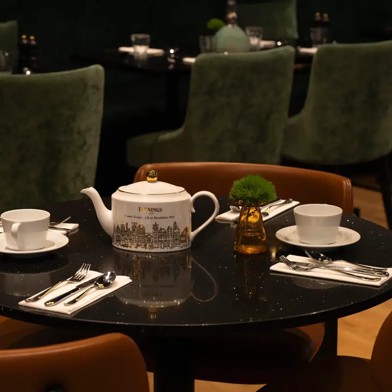 Twinings tekanne plassert på et rundt bord i en restaurant dekket med hvite kopper og bestikk.