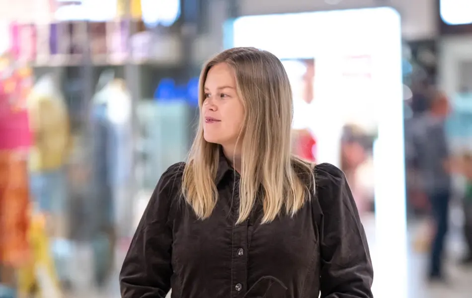 Jente med blondt hår, har på seg en knelang brun kjole med knapper og knytebelte i livet.