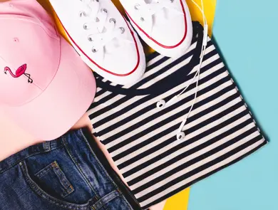 Fashion blogger concept. Summer sport, recreation and travel outfit: striped t-shirt, denim shorts, pink hat, white snickers. Minimal set of feminine teen clothes on pastel background